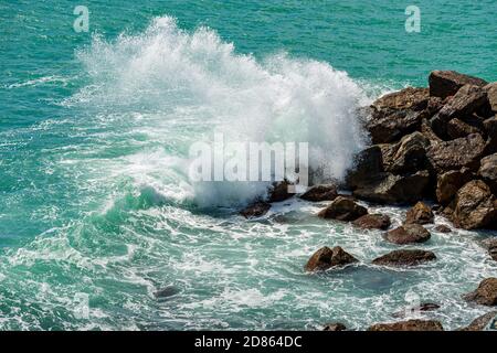 Le onde bianche del mare verde si infrangono sulle rocce. Breakwater nel Golfo di la Spezia, Liguria, Italia Foto Stock