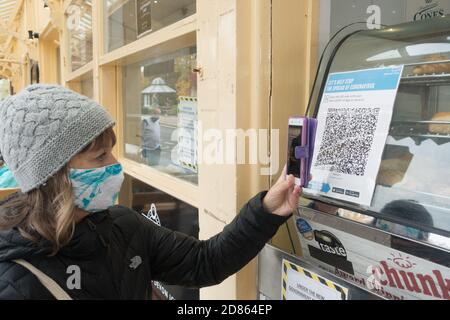 Una donna con maschera facciale utilizza il suo smartphone per eseguire la scansione del codice QR NHS per entrare in un luogo per il sistema di traccia e traccia. Foto Stock