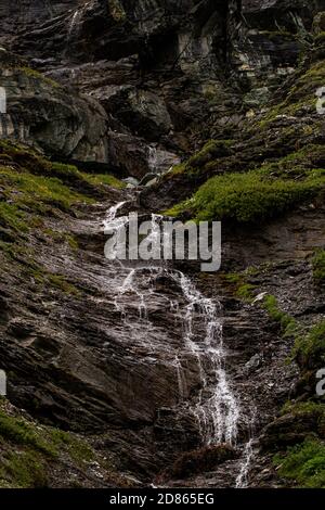 Una cascata cade accanto a una grotta scura, che si conpozza in una volta cascata limpida. Alpi svizzere Foto Stock