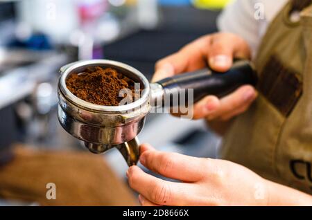 Primo piano del barista femminile che tiene il caffè macinato a mano per la preparazione di espresso, servizio e concetto di preparazione. Foto Stock