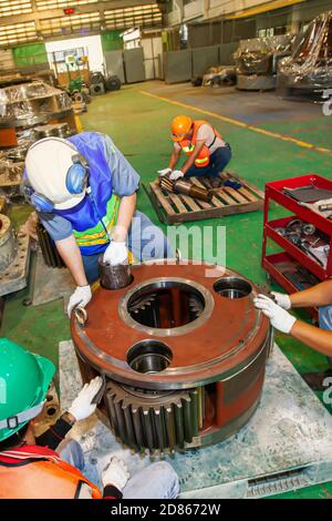 Un gruppo di tecnici che indossano dispositivi di protezione ripara le ruote dentate del motore grandi in fabbrica. Vista dall'alto. Chiudi. Foto Stock