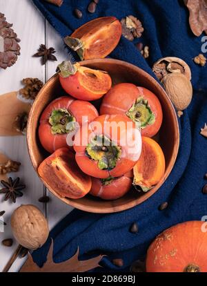 regali di autunno, vista dall'alto, persimmons maturi in una ciotola di legno su uno sfondo con noci, foglie e un cono di pino Foto Stock