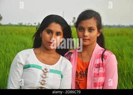 Primo piano di due ragazze adolescenti con capelli lunghi che indossano abiti bianchi e rosa con rossetto in un campo di risaie, messa a fuoco selettiva Foto Stock