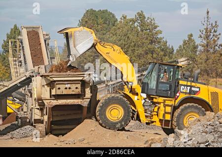 Un trattore grande e movimento terra in un cantiere a Bend, Oregon, sposta i massi in un frantumatore di rocce per fare ghiaia. Il cantiere è per Foto Stock