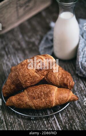 Vista sui croissant appena sfornati su un tavolo di legno con bottiglia di latte in background semplice colazione del mattino Foto Stock