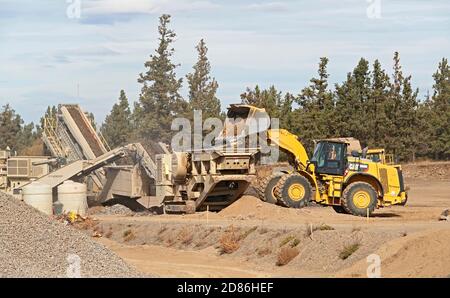 Un trattore grande e movimento terra in un cantiere a Bend, Oregon, sposta i massi in un frantumatore di rocce per fare ghiaia. Il cantiere è per Foto Stock