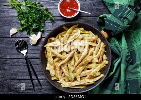 Fagioli francesi di cera d'oro con aglio e prezzemolo ricoperti di pangrattato e fritti su una padella su uno sfondo di legno scuro con ketchup, vista dall'alto, clo Foto Stock