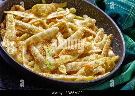 Piatto vegetariano: Fagioli di cera d'oro francesi con aglio e prezzemolo ricoperti di pangrattato e fritti su una padella su fondo di legno scuro, vista dall'alto, Foto Stock