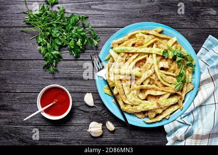 Fagioli di cera a basso contenuto calorico alla francese d'oro con aglio e prezzemolo ricoperti di pangrattato e fritti su una padella, serviti su un piatto blu con forchetta al buio Foto Stock