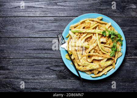 Fagioli di cera a basso contenuto calorico alla francese d'oro con aglio e prezzemolo ricoperti di pangrattato e fritti su una padella, serviti su un piatto blu con forchetta al buio Foto Stock