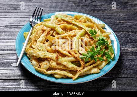 Fagioli di cera a basso contenuto calorico alla francese d'oro con aglio e prezzemolo ricoperti di pangrattato e fritti su una padella, serviti su un piatto blu con forchetta al buio Foto Stock