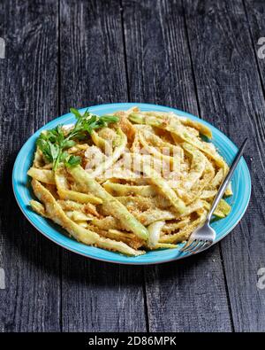 Fagioli di cera a basso contenuto calorico alla francese d'oro con aglio e prezzemolo ricoperti di pangrattato e fritti su una padella, serviti su un piatto blu con forchetta al buio Foto Stock