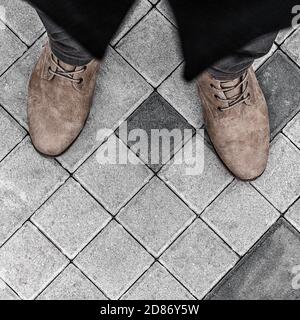 primo piano del corpo inferiore di un uomo in un cappotto nero, jeans e stivali in pelle beige, contro uno sfondo grigio pavement Foto Stock