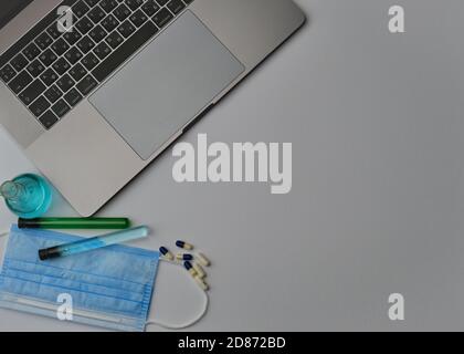 Flatlay di computer portatile, tubi medici e fiasca, maschera e occhiali su una scrivania grigia. Lavorare da casa. Virus e autoisolamento Foto Stock