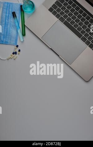 Flatlay di computer portatile, tubi medici e fiasca, maschera e occhiali su una scrivania grigia. Lavorare da casa. Virus e autoisolamento Foto Stock