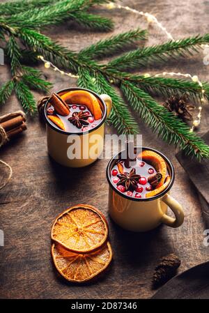 VIN brulé natalizio con mirtilli rossi, arancio e spezie in tazze su sfondo rustico in legno compensato. Bevanda calda invernale tradizionale. Foto Stock