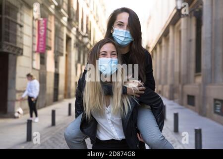 Due ragazze che si divertono per strada. Indossano maschere mediche. Foto Stock