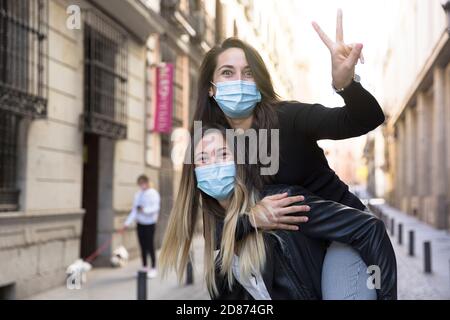 Due ragazze che si divertono per strada. Indossano maschere mediche. Foto Stock