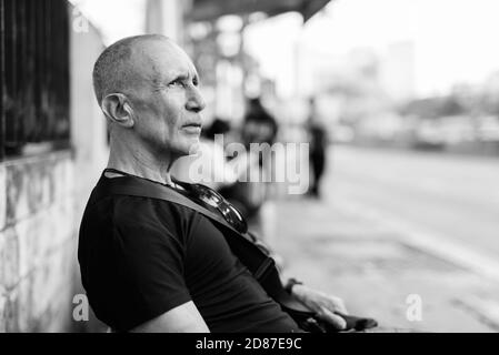 Vista di profilo di bald senior uomo turistica pensando in attesa presso la fermata del bus a Bangkok in Tailandia Foto Stock