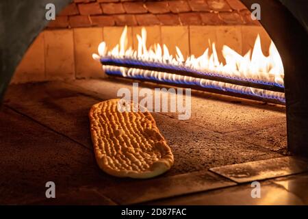 Cucina turca, pane pita in mattoni di pietra forno a fiamma naturale su tavola di legno, pane caldo fresco cotto, spazio copia. Immagine concettuale di panetteria o panetteria. Foto Stock