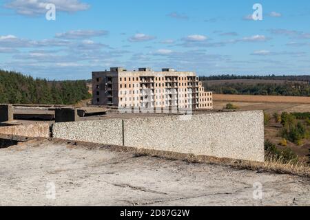 Vista dal tetto in cemento di alto edificio sovietico abbandonato a più piani con vista su un'altra casa con un paesaggio blu luminoso. Città incompiuta di nuclei Foto Stock