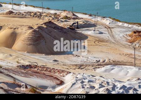 Estrazione della sabbia con macchina scavatrice in cava di quarzo. Dune di sabbia colline terreno scavare vicino lago Foto Stock