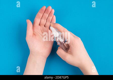Vista dall'alto della foto di una donna mani con l'applicazione di spray dal flacone piccolo su mani isolate su sfondo blu di colore brillante Foto Stock