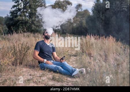 Bell'uomo vape godendo di un dispositivo elettronico di fumo sull'erba. Non fumatori. Foto Stock