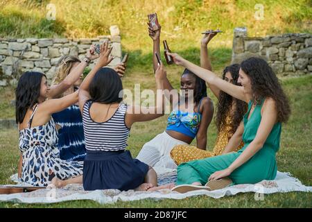 Gruppo di amici donne che bevono birra e alzano i loro smartphone Foto Stock