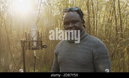 Giovane uomo nero afroamericano che canta nel microfono nei boschi. Luce naturale. Foto di alta qualità Foto Stock