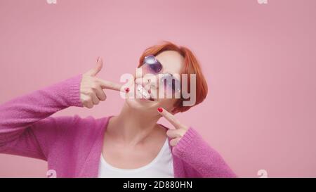 Attraente donna di mezza età con i capelli rossi che puntano le dita sui suoi denti bianchi. Foto di alta qualità Foto Stock