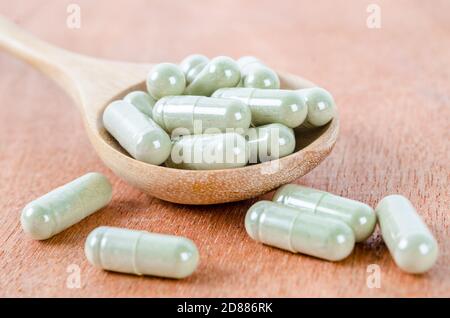 Capsule mediche di erbe in cucchiaio di legno su sfondo di legno. Foto Stock