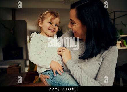 Mamma e figlia allegre che giocano e ridono a causa del solletico in piedi in salotto a casa