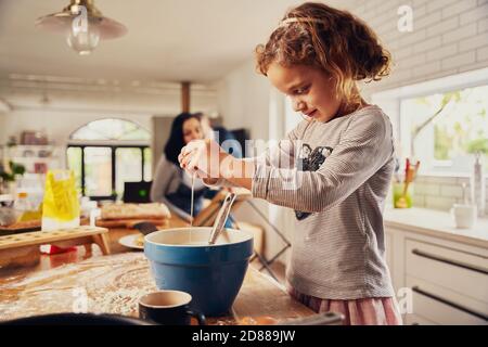 Carino bambina bambino rompere l'uovo in una ciotola mentre preparare l'impasto in un bancone da cucina disordinato a casa Foto Stock