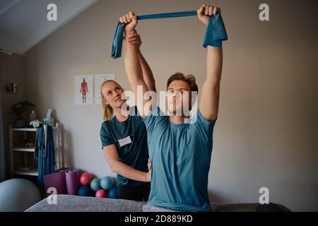 Ritratto di un giovane che fa esercizi con l'aiuto di terapeuta in ufficio medico con elastico Foto Stock
