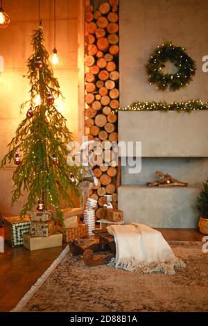 Interni natalizi nello stile di un loft scandinavo: Cemento grigio, decorazioni in legno, lampade incandescenti, albero di Natale artificiale realistico. Nuovo e accogliente Foto Stock