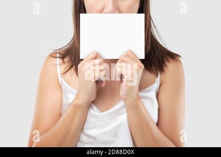 Una donna in abito satinato bianco che tiene una carta bianca bianca su uno sfondo grigio chiaro. Foto Stock