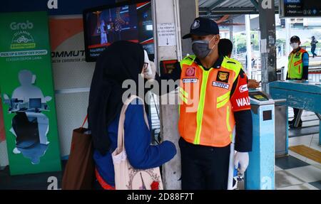 Depok, Indonesia - 18 marzo 2020: Gli agenti di sicurezza controllano la temperatura corporea dei passeggeri all'ingresso della stazione ferroviaria di Depok per prevenire il Foto Stock