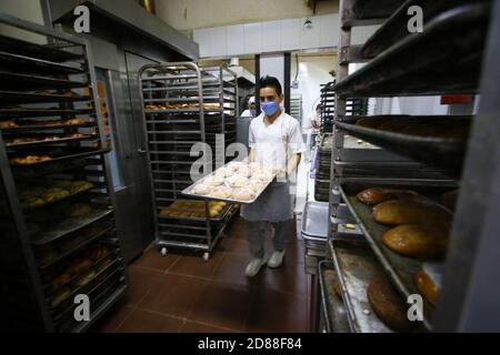 Città del Messico, Messico. 27 Ott 2020. Un panettiere toglie appena fatto 'pan de muerto', o un tipo di pane tradizionale messicano, in una panetteria a Città del Messico, capitale del Messico, 27 ottobre 2020. Fare 'pan de muerto' è una delle più importanti tradizioni del giorno dei morti celebrazioni. Credit: Montserrat Lopez/Xinhua/Alamy Live News Foto Stock