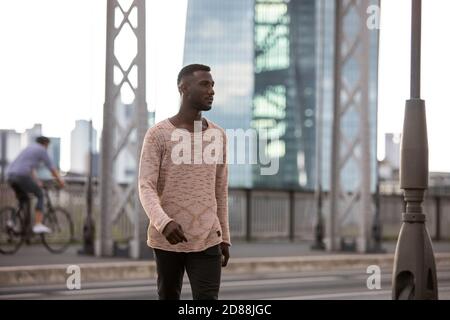 Uomo nero alla moda che cammina sulla strada con la testa girata a lato. Tre quarti di lunghezza. Foto Stock