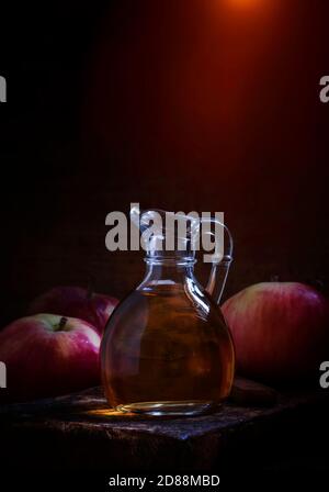 Aceto di sidro di mele in caraffa di vetro, mele fresche, tavolo vecchio in legno, tasto basso, fuoco selettivo Foto Stock
