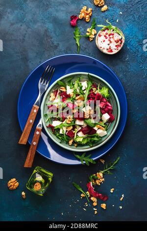 Insalata estiva di barbabietole con rucola, radicchio, formaggio morbido e noci su piatto con forchetta, condimento e spezie su tavolo da cucina blu, spazio copia, vista dall'alto Foto Stock