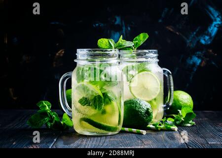 Tè verde freddo con lime e menta in vasetti di vetro, sfondo scuro, fuoco selettivo Foto Stock