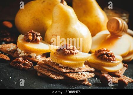 Antipasto da pane scuro croccante, formaggio di cottage, noci e pere con miele, sfondo scuro, fuoco selettivo Foto Stock