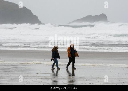 Newquay, Cornovaglia, Regno Unito. 28 ottobre 2020. Regno Unito Meteo. Una coppia lotta per camminare nei forti venti gustosi sulla spiaggia di Fistral come grandi onde dai resti dell'uragano Epsilon crash a Newquay in Cornovaglia durante le vacanze scolastiche di metà periodo. Picture Credit: Graham Hunt/Alamy Live News Foto Stock