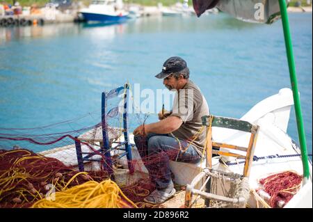 Pescatori greci che minacciano reti sulla banchina di Georgiouploi in Creta con barche sullo sfondo Foto Stock