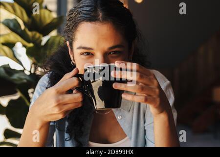 Primo piano di una giovane donna che beve caffè al bar. Femmina con una tazza di caffè. Foto Stock