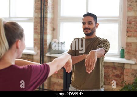 Giovane uomo che ripete il movimento per l'istruttore durante l'addestramento in centro benessere Foto Stock