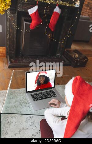 Vista posteriore di donna in cappello di santa con una videocamera con un'altra donna nel cappello di santa sorridente sul laptop Foto Stock