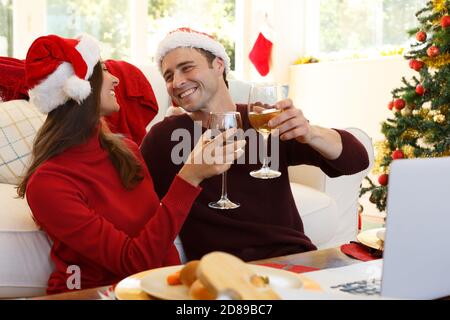 Coppia che indossa il cappello di santa guardando l'un l'altro sorridendo e. tostatura mentre si è seduti in soggiorno Foto Stock